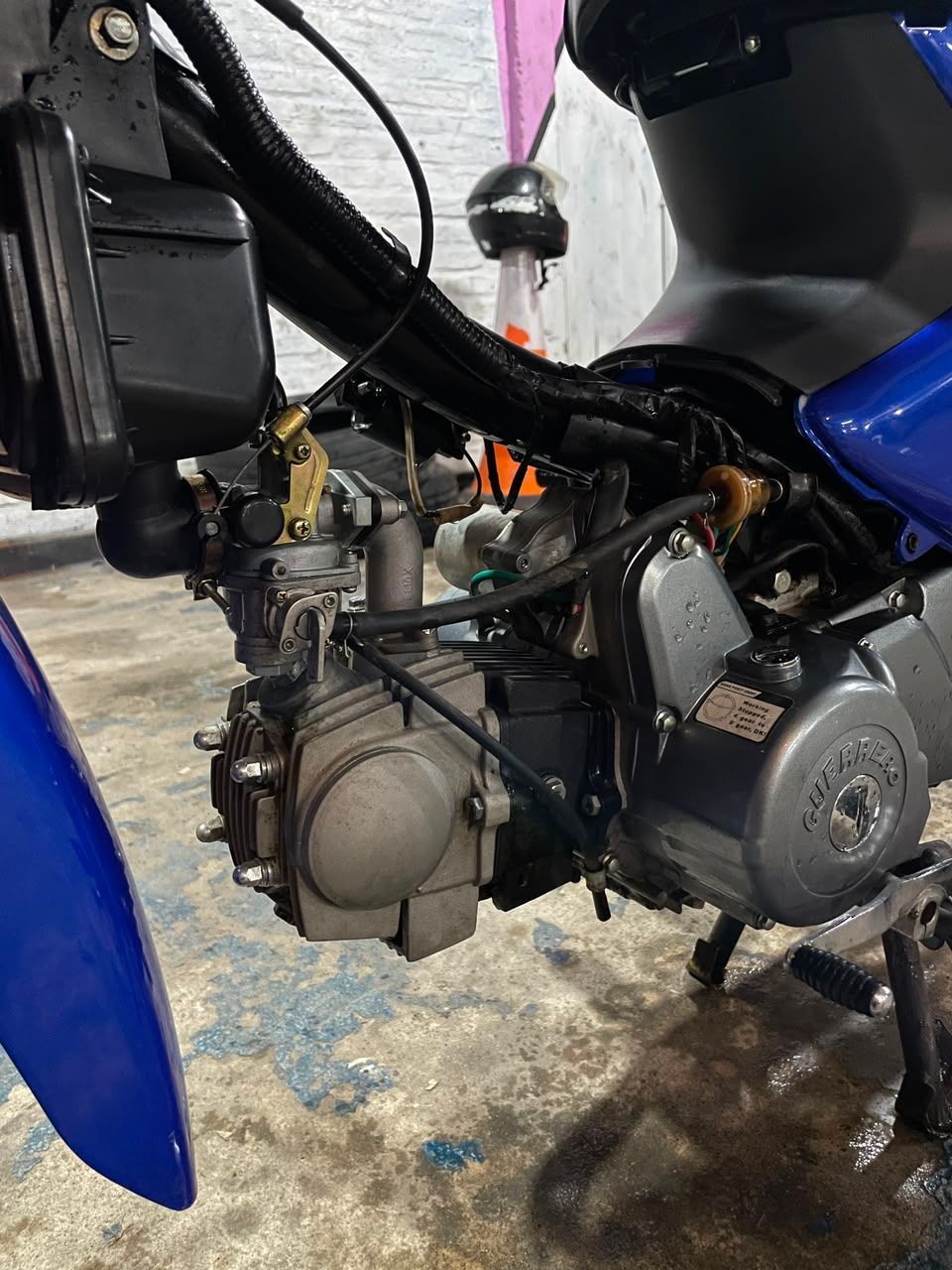 Primer plano del motor y el chasis de una motocicleta azul, con el cableado y las piezas mecánicas visibles.