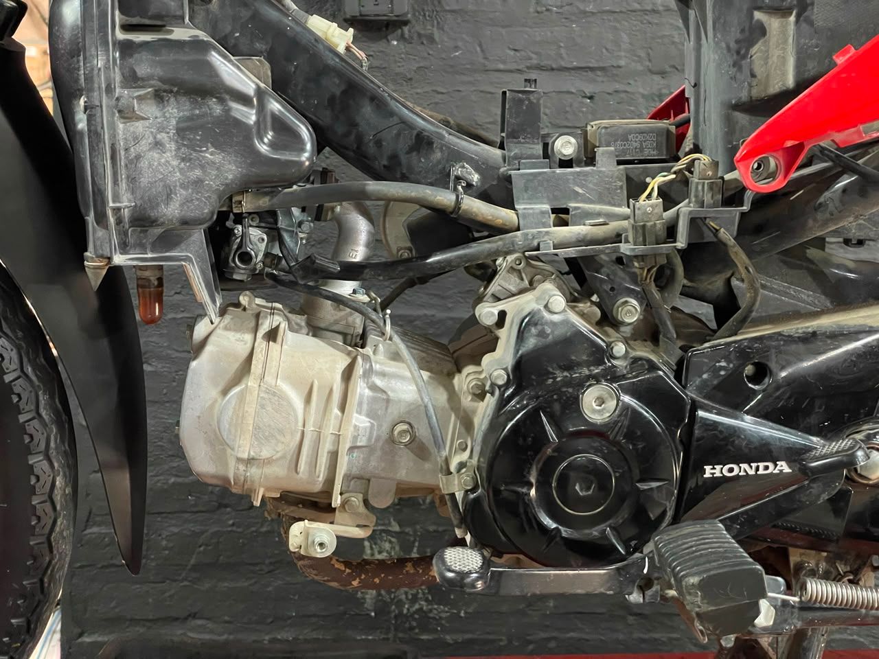 Motor y chasis de motocicleta Honda dañados, con partes expuestas, contra una pared oscura.