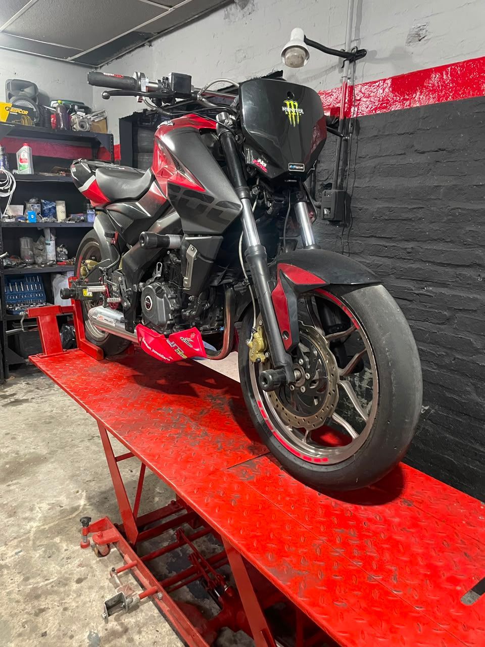 Motocicleta deportiva negra sobre un elevador rojo en un garaje, vista frontal de tres cuartos.