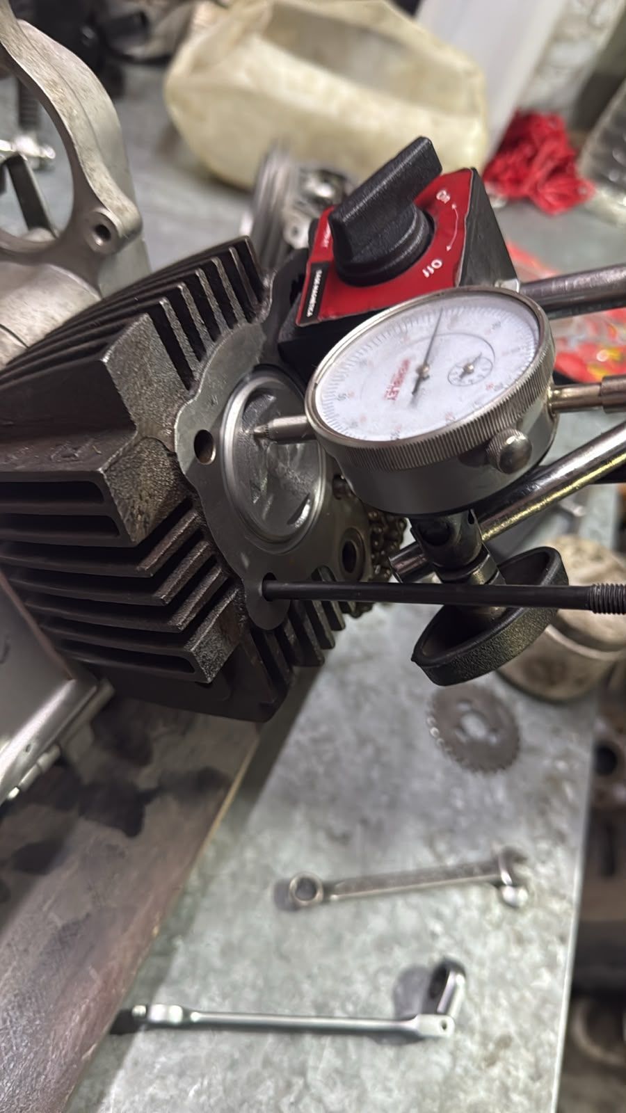 Comparador de cuadrante en la culata de un motor pequeño en un taller, con llaves inglesas cerca.