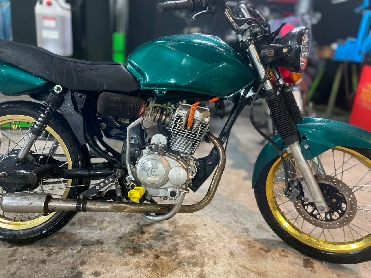 Motocicleta personalizada de color turquesa con ruedas doradas estacionada en un garaje o taller.
