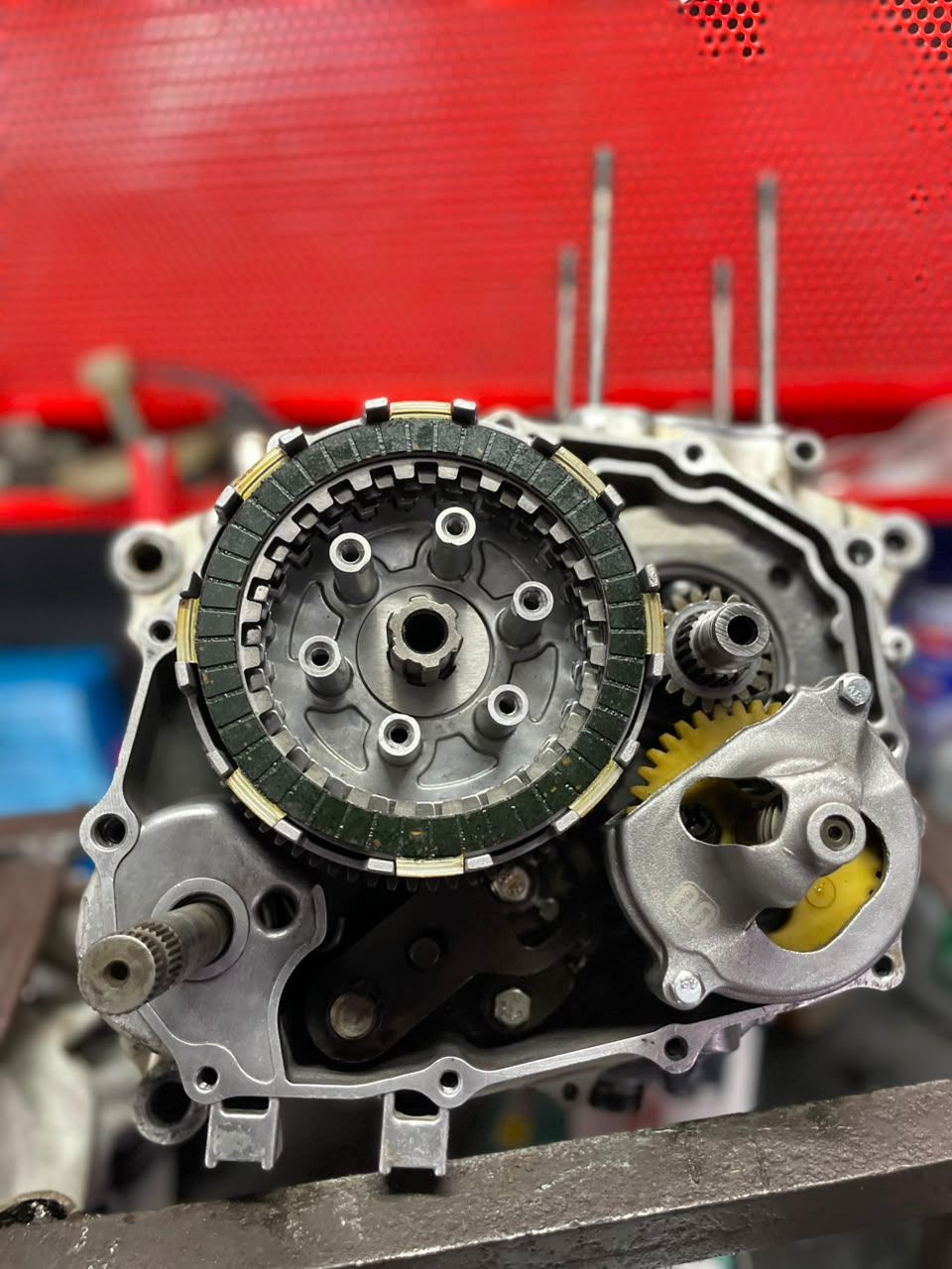 Primer plano de un conjunto de motor expuesto con engranajes y componentes metálicos sobre un fondo rojo.