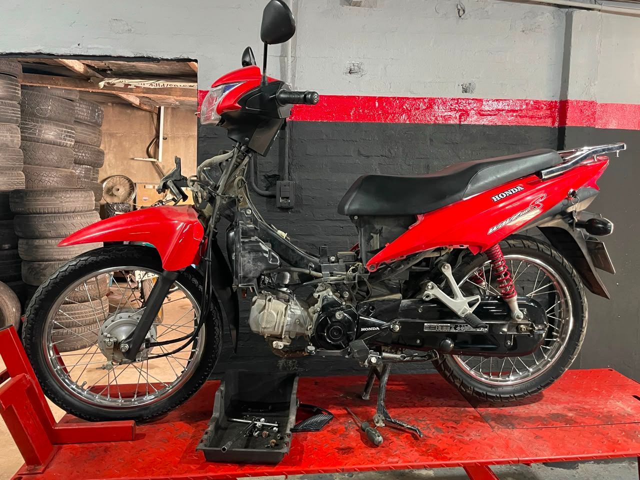 Motoneta roja sobre una plataforma roja en un taller que parece un garaje.