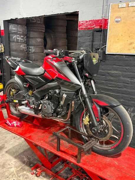 Motocicleta deportiva roja y negra sobre un elevador en un garaje, con neumáticos apilados al fondo.