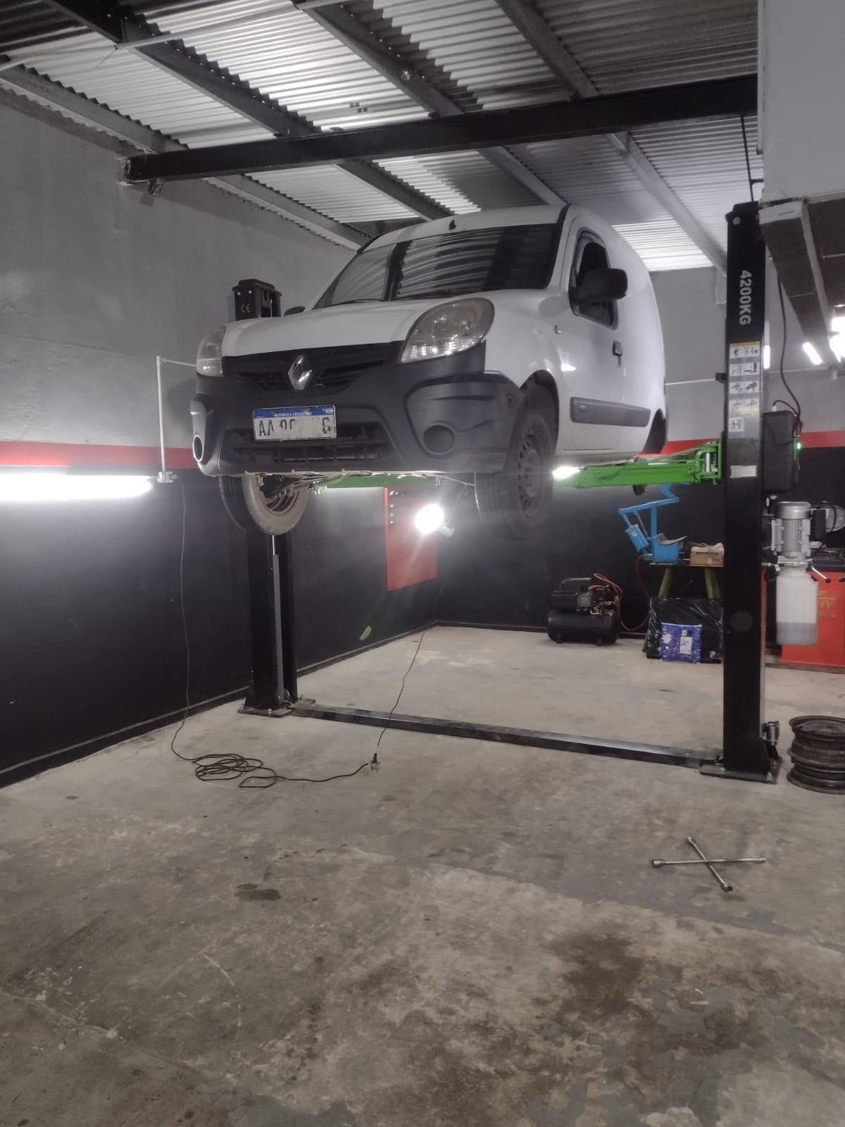 Una furgoneta blanca elevada sobre un elevador de coches de dos columnas en un taller de reparación de automóviles.