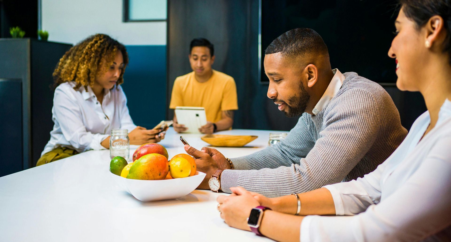 Un grupo de personas está sentado alrededor de una mesa con un bol de fruta.