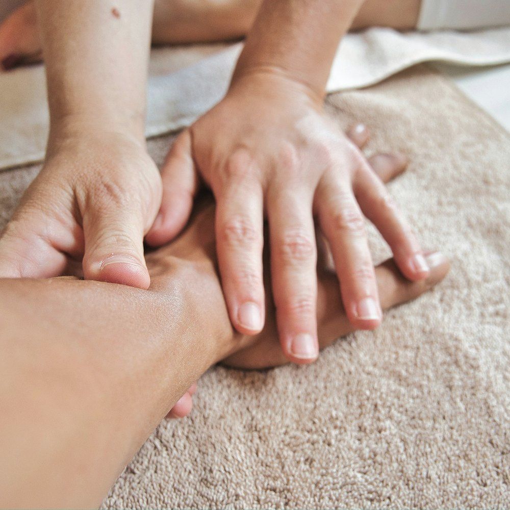 A patient lying comfortably under a sheet while slow, light strokes are worked along the arm.