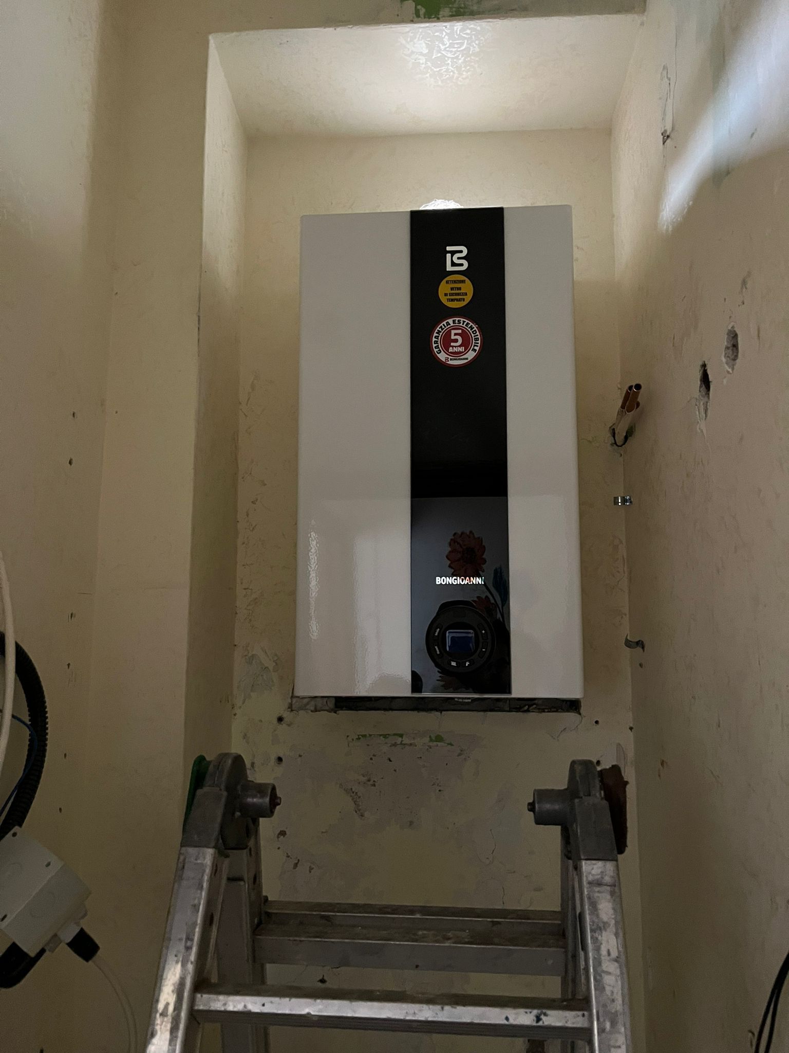 Una scala è appoggiata accanto a una scatola bianca su un muro.