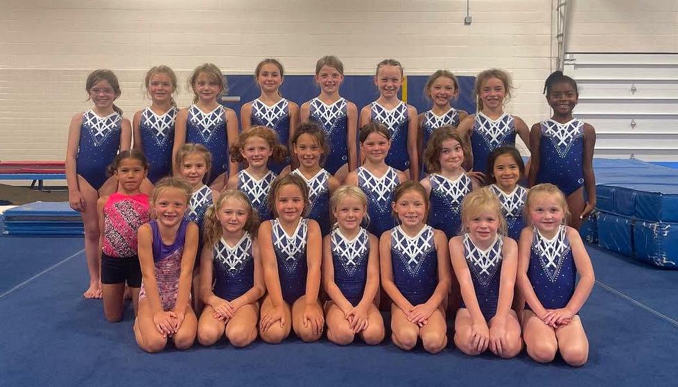 Gymnastics team posing in blue leotards on a gym floor.