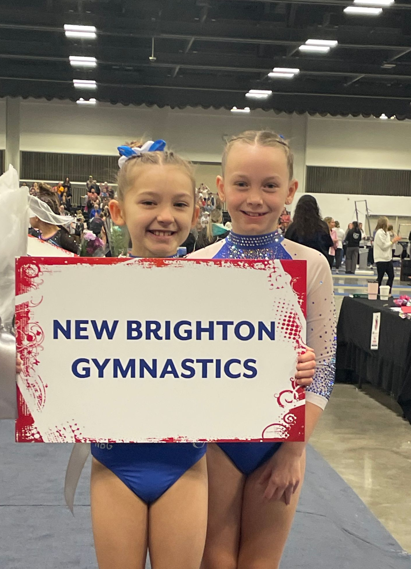 Two young gymnasts in blue leotards hold a
