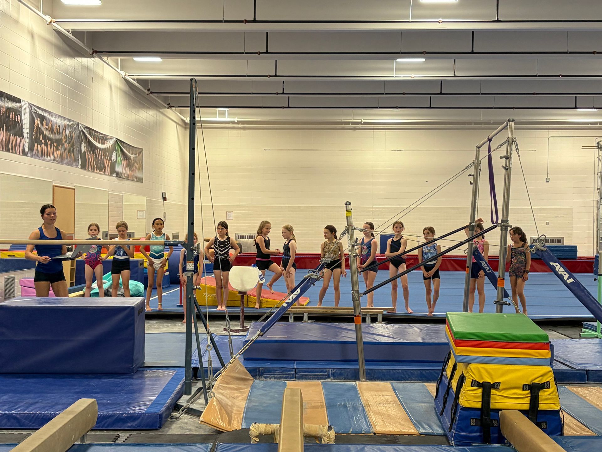 Gymnastics practice in a gym, with athletes on bars and mats during training.