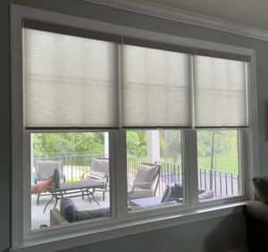service Three window shades partially covering a window that looks out onto a patio with furniture.