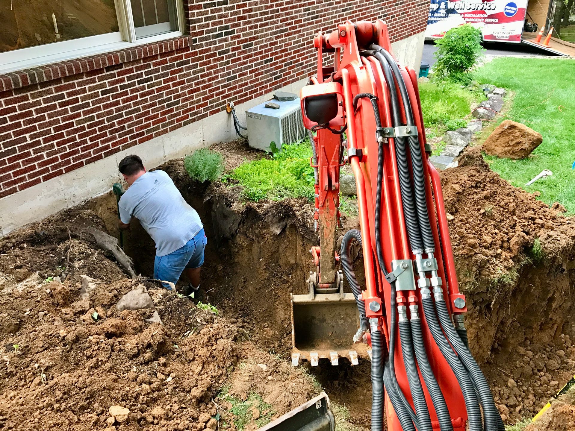 Worker digging beside brick house with an excavator in a muddy trench