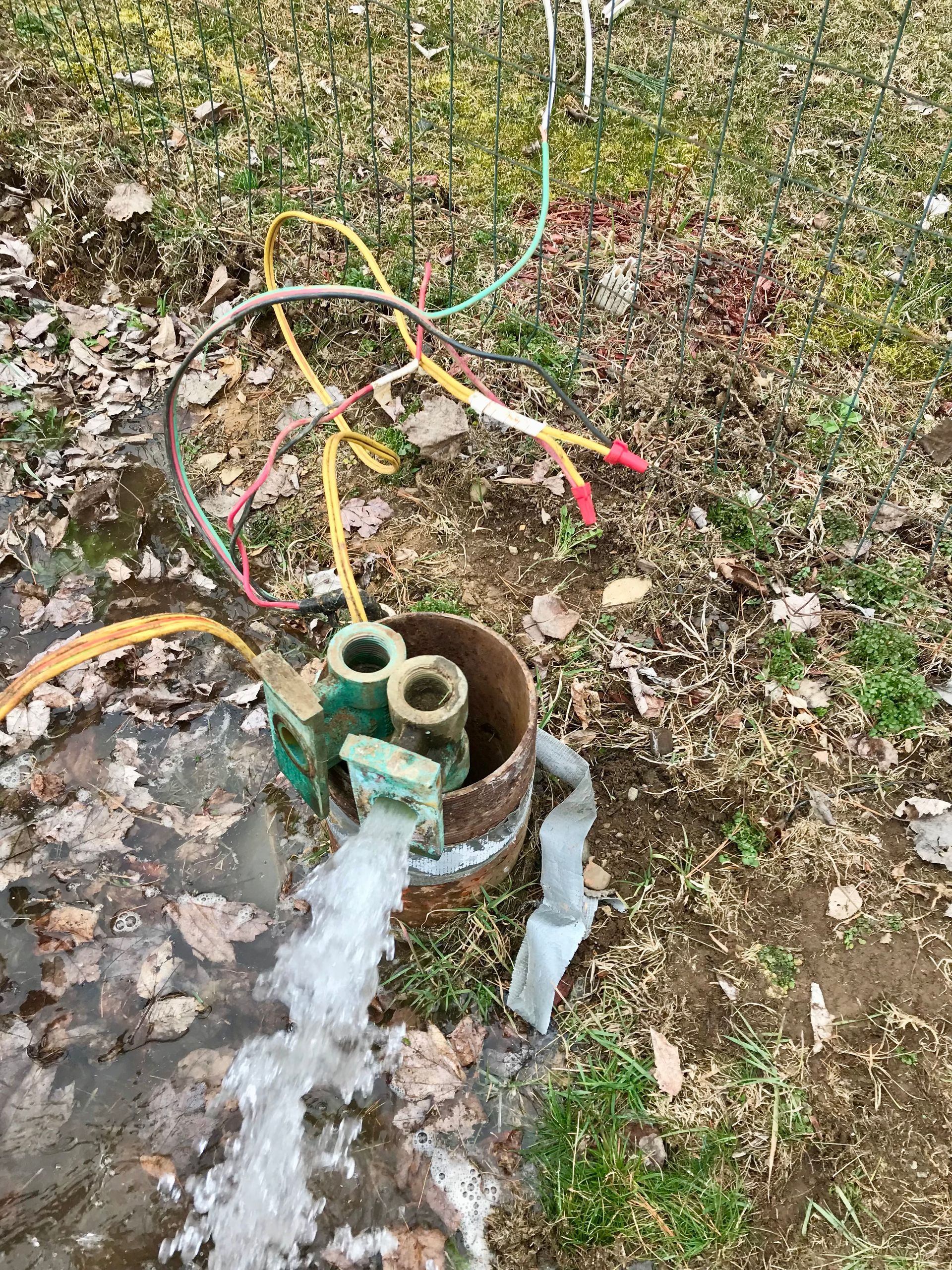 Damaged outdoor water pipe with hoses spraying water onto muddy ground and grass