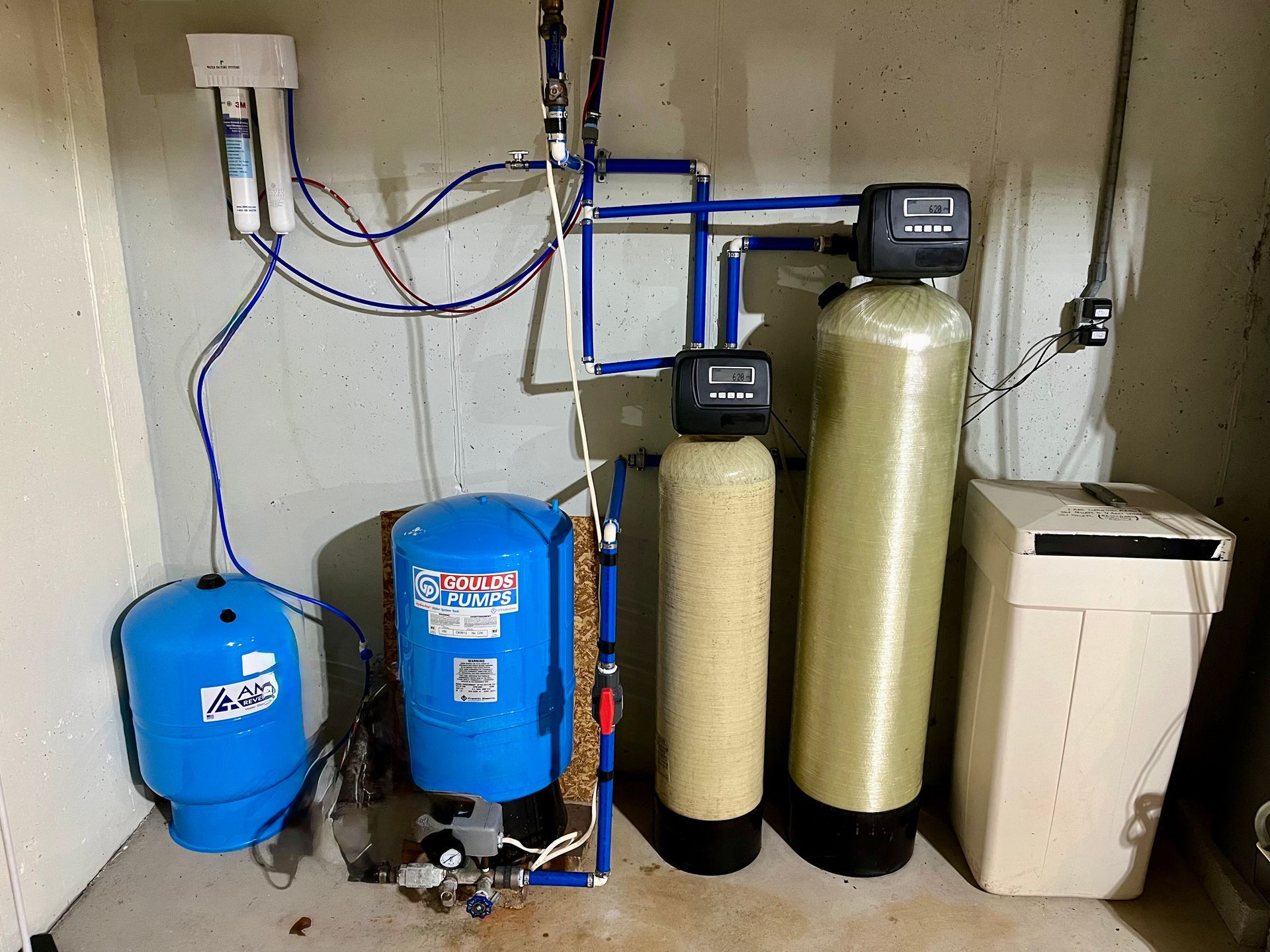 Water softening and filtration equipment with blue and beige tanks installed in a utility room