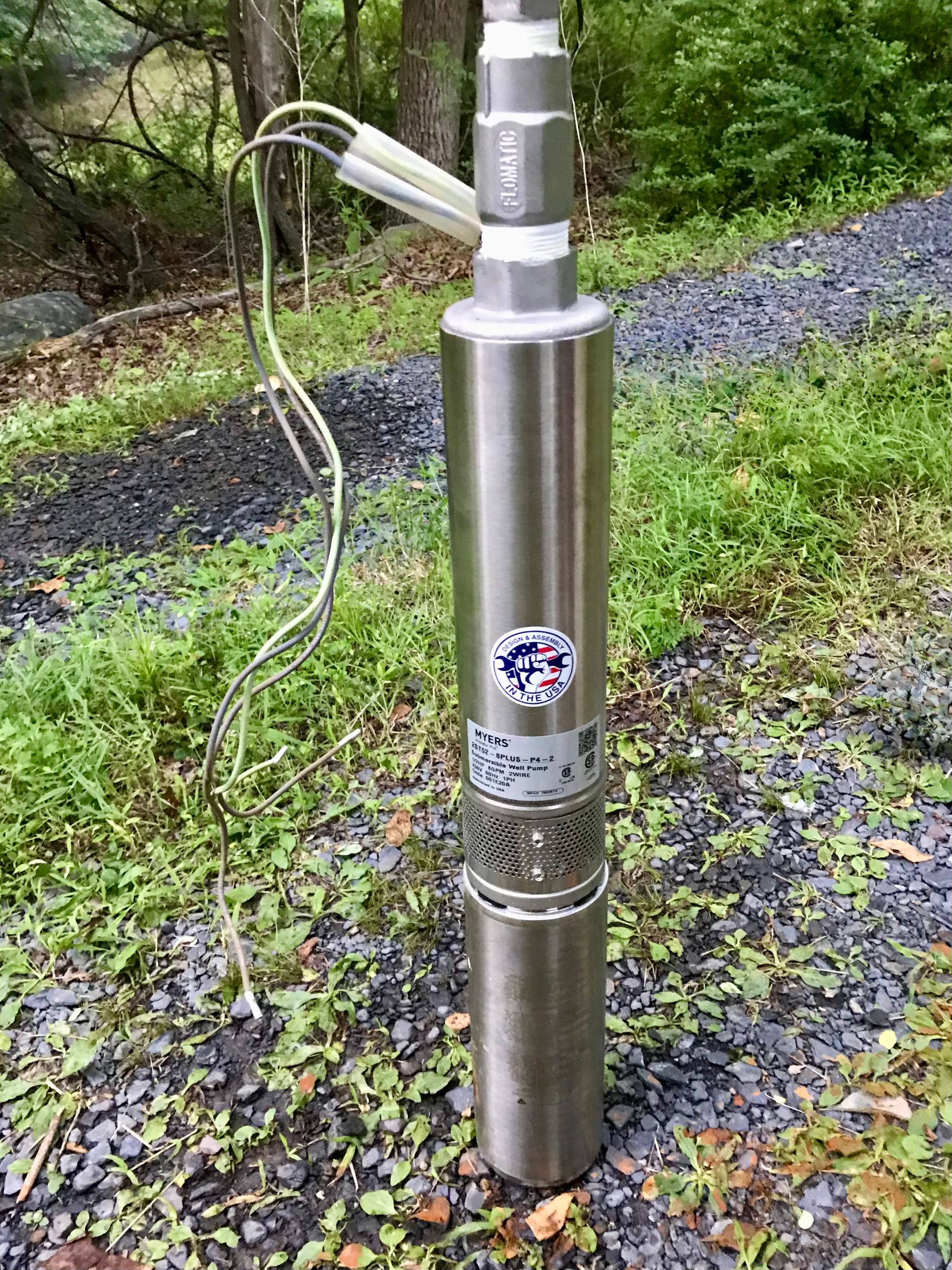 Stainless steel outdoor utility post with attached cable in grassy woodland area