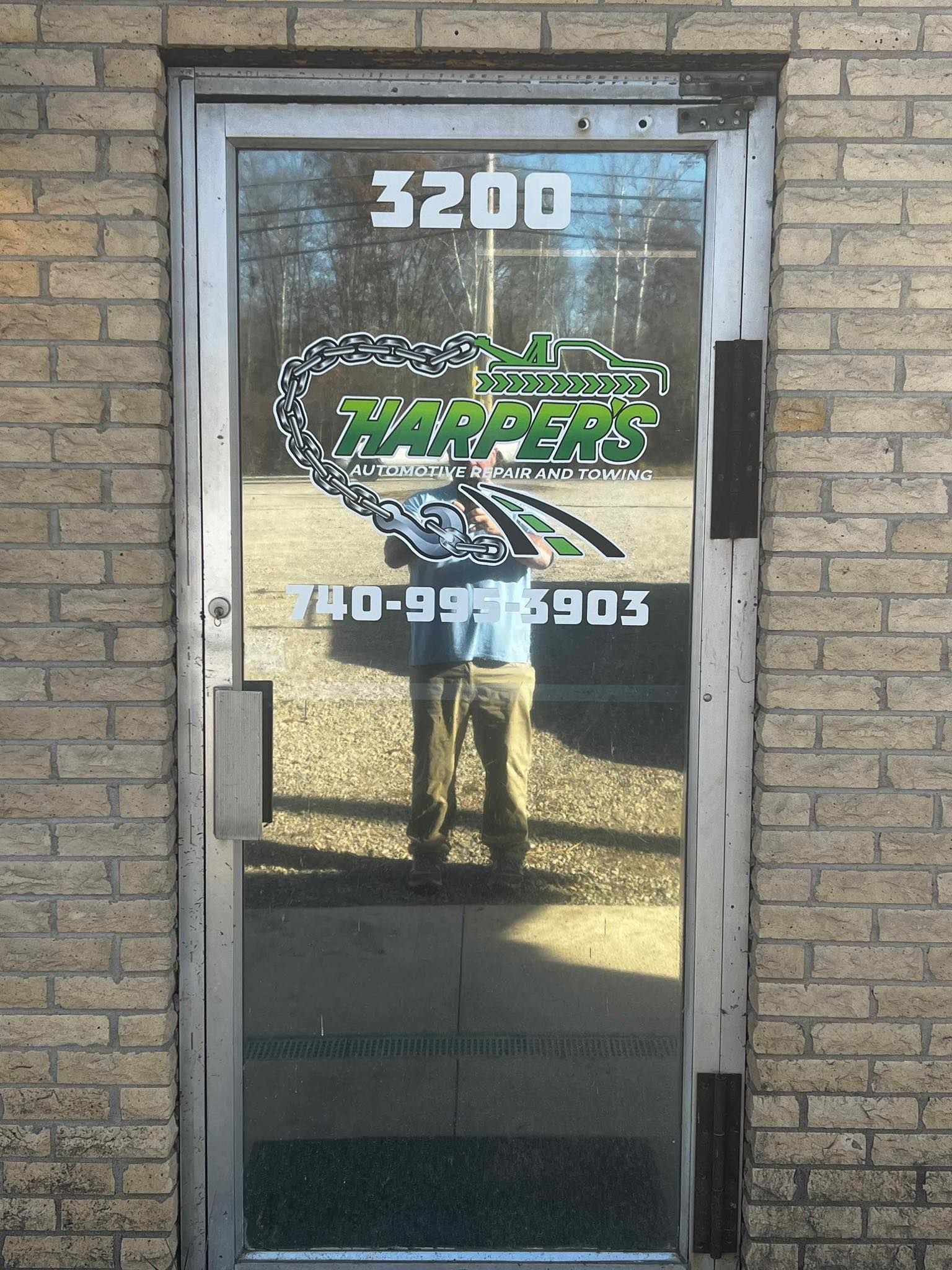 Glass storefront door with green logo, street number 3200, and reflections of a person outside.