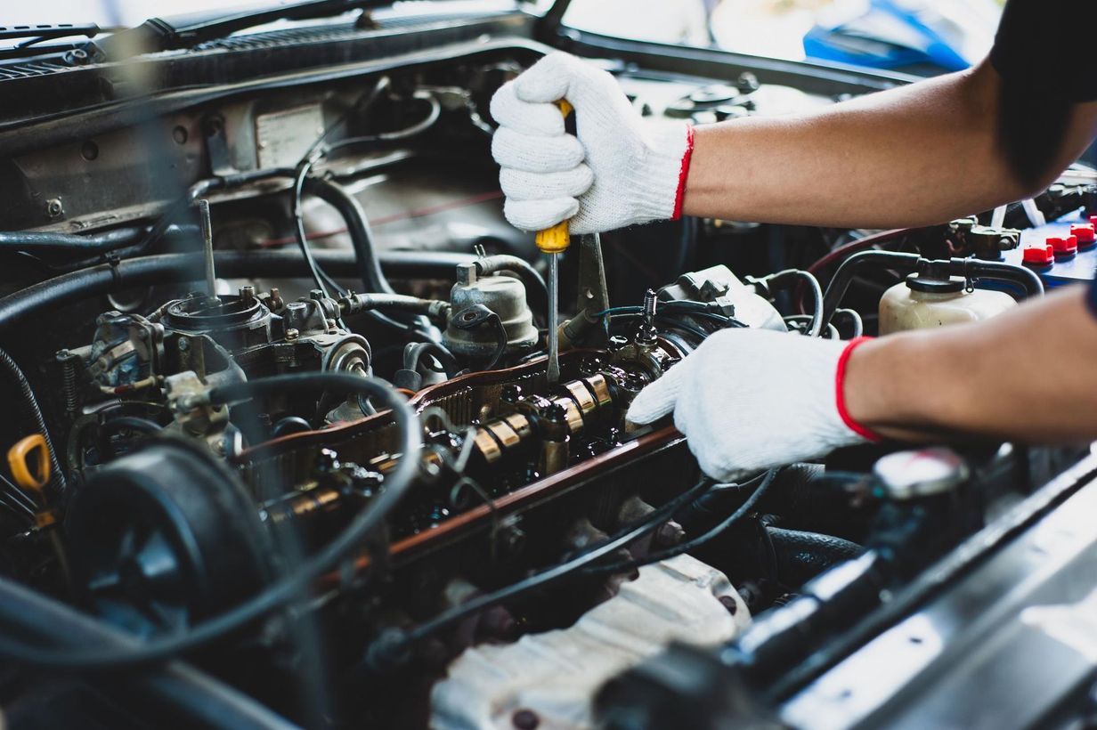 Mechanic wearing white gloves working under a car hood with tools and exposed engine components