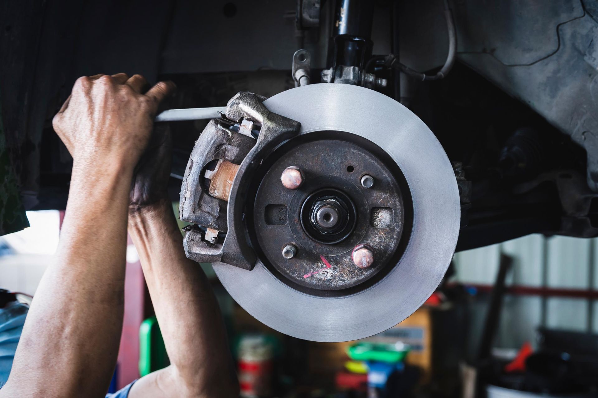 Mechanic working on a car’s front brake disc and caliper in a garage