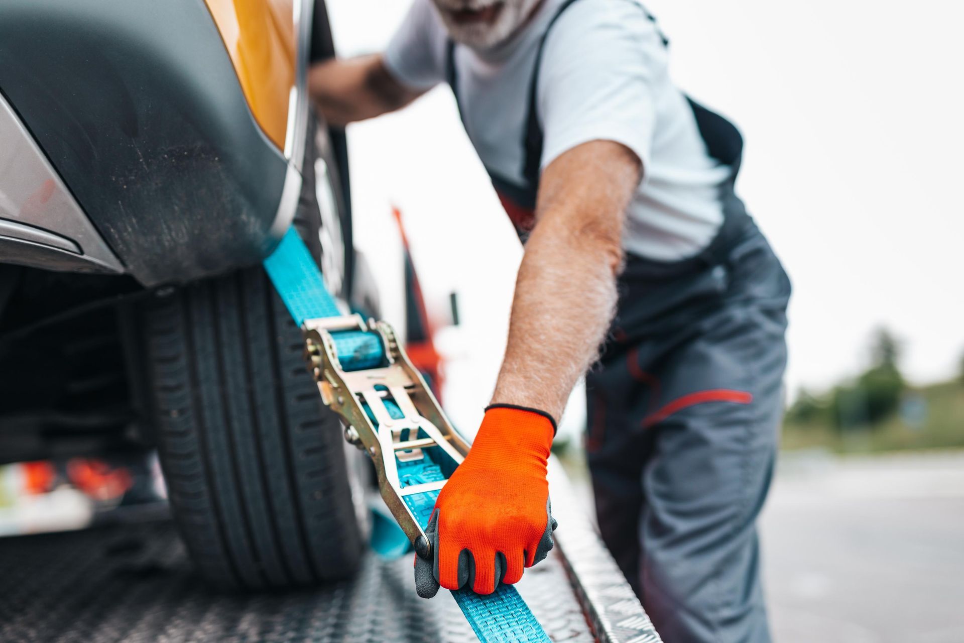 Person tightening a blue tow strap to a car wheel on a roadside tow truck platform