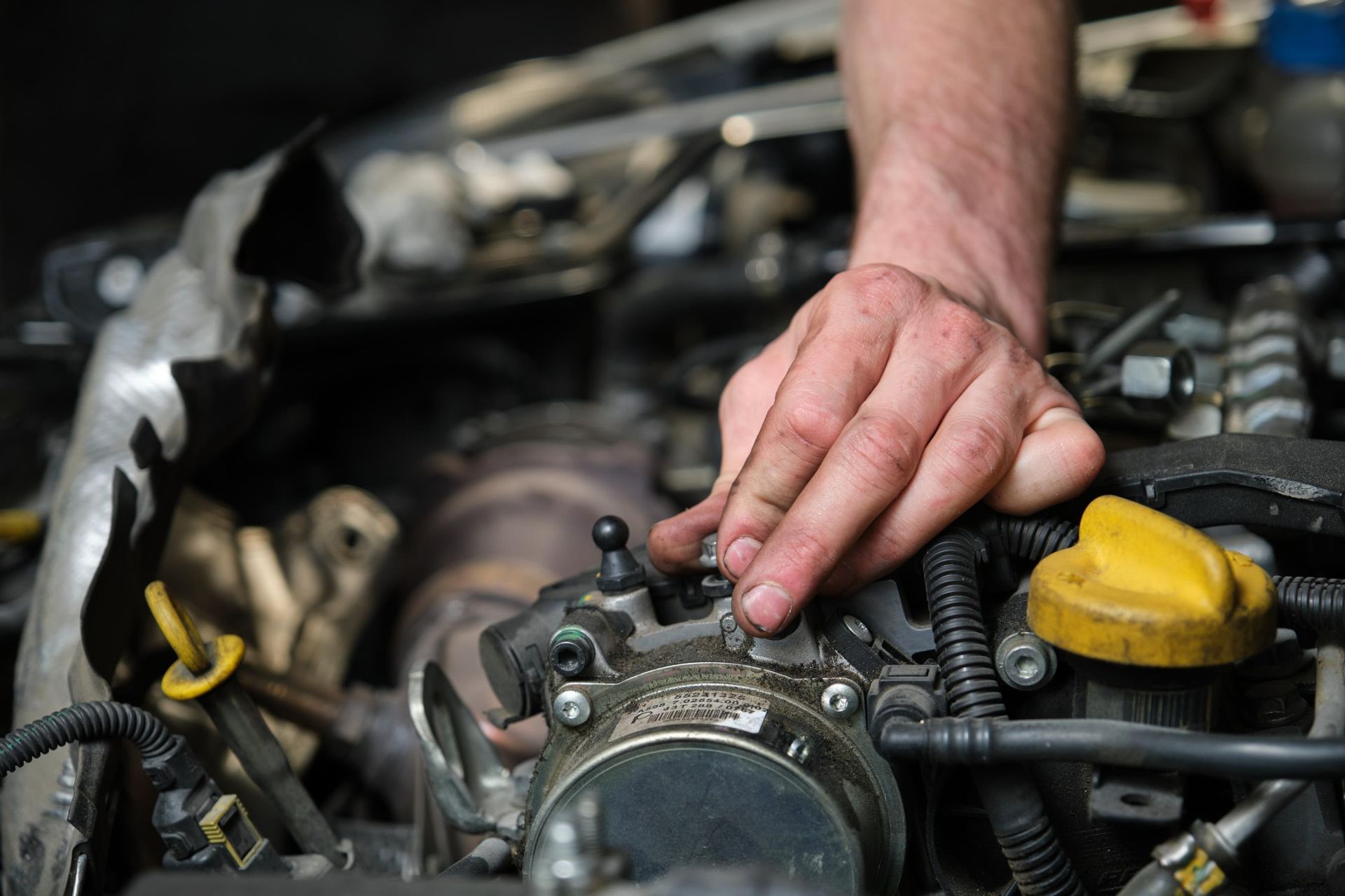 Hand tightening a car engine component under the hood, with a yellow oil cap nearby