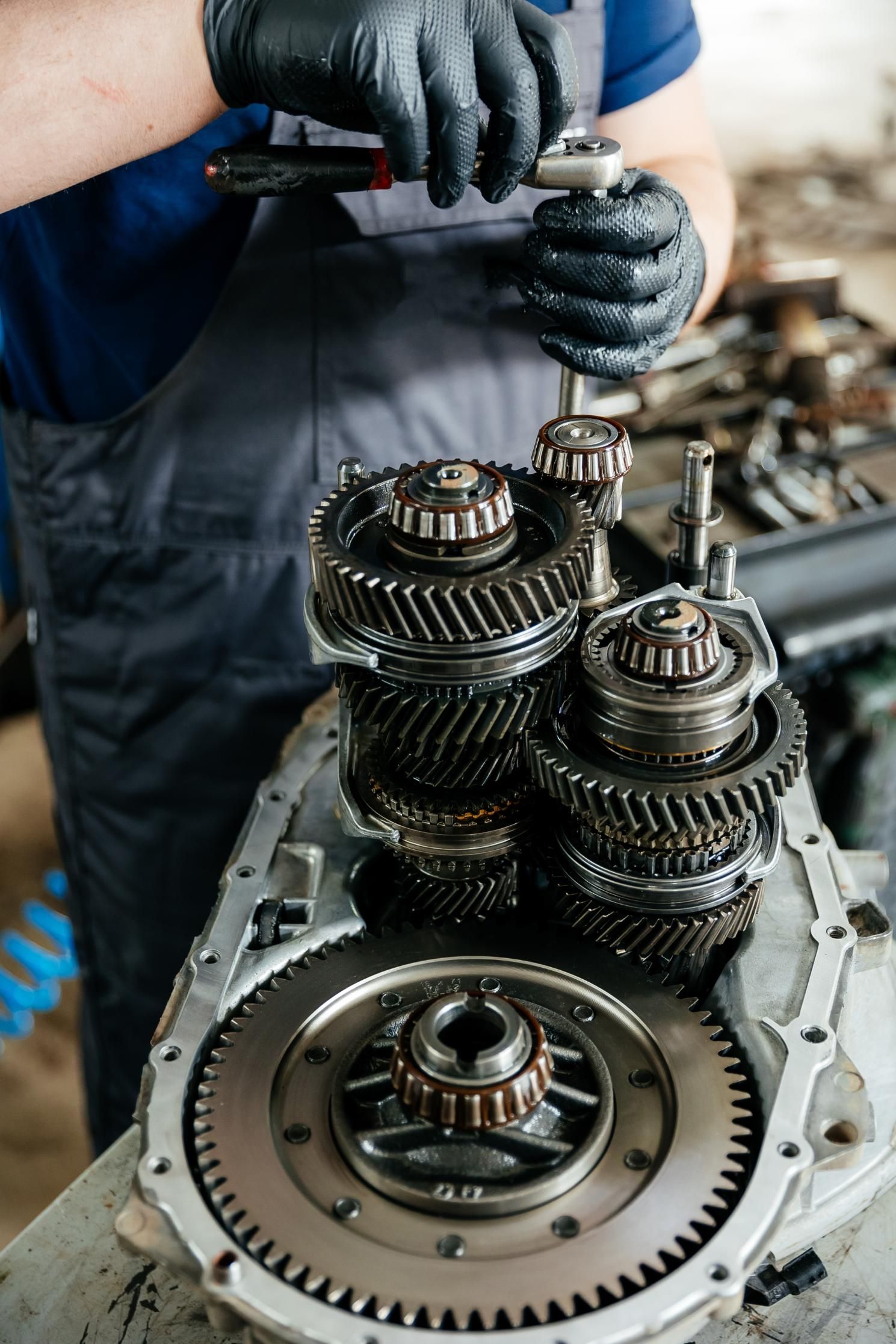 Mechanic in gloves working on exposed transmission gears inside an engine casing.