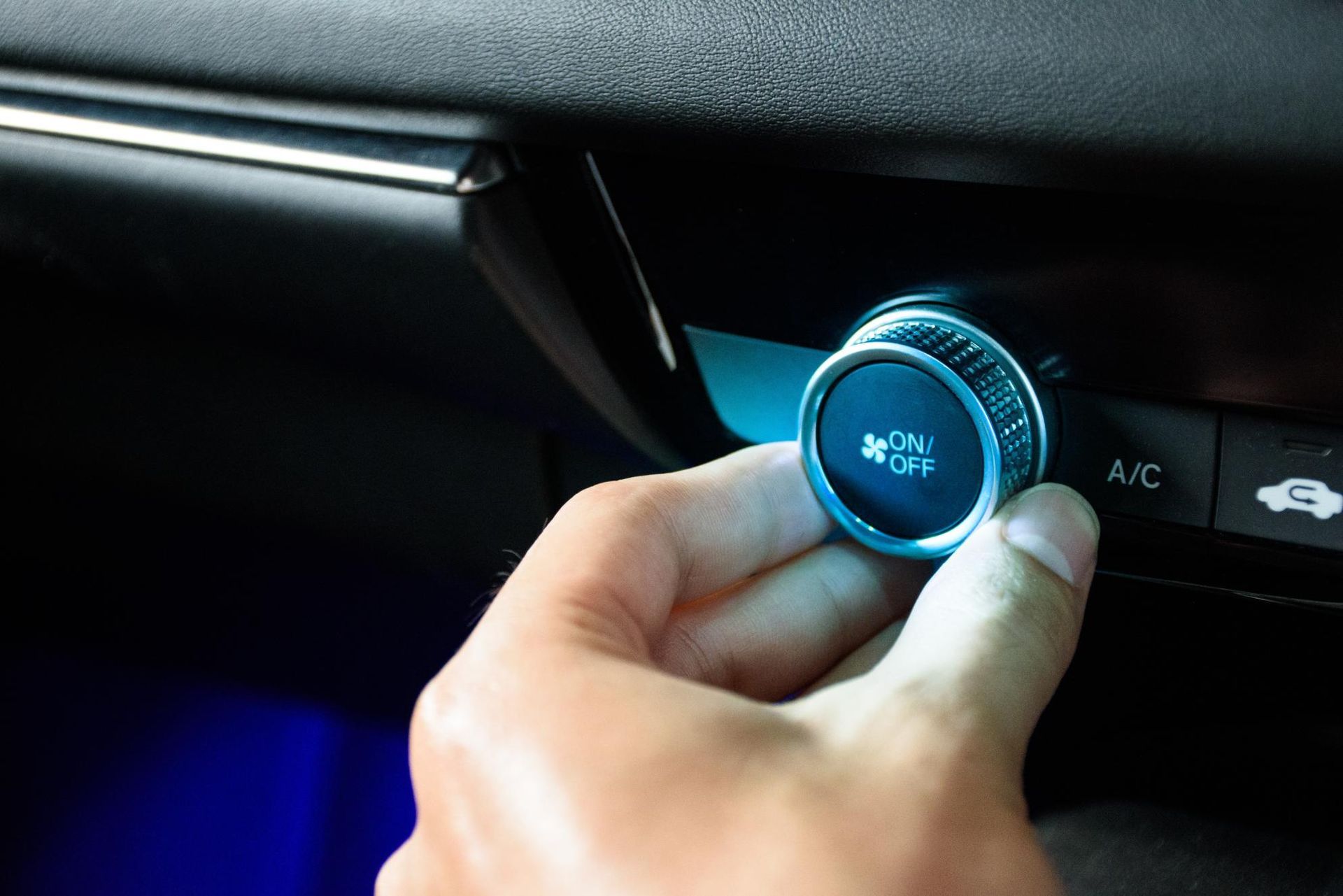 Hand adjusting a car climate control knob with blue illuminated ring and A/C icons nearby