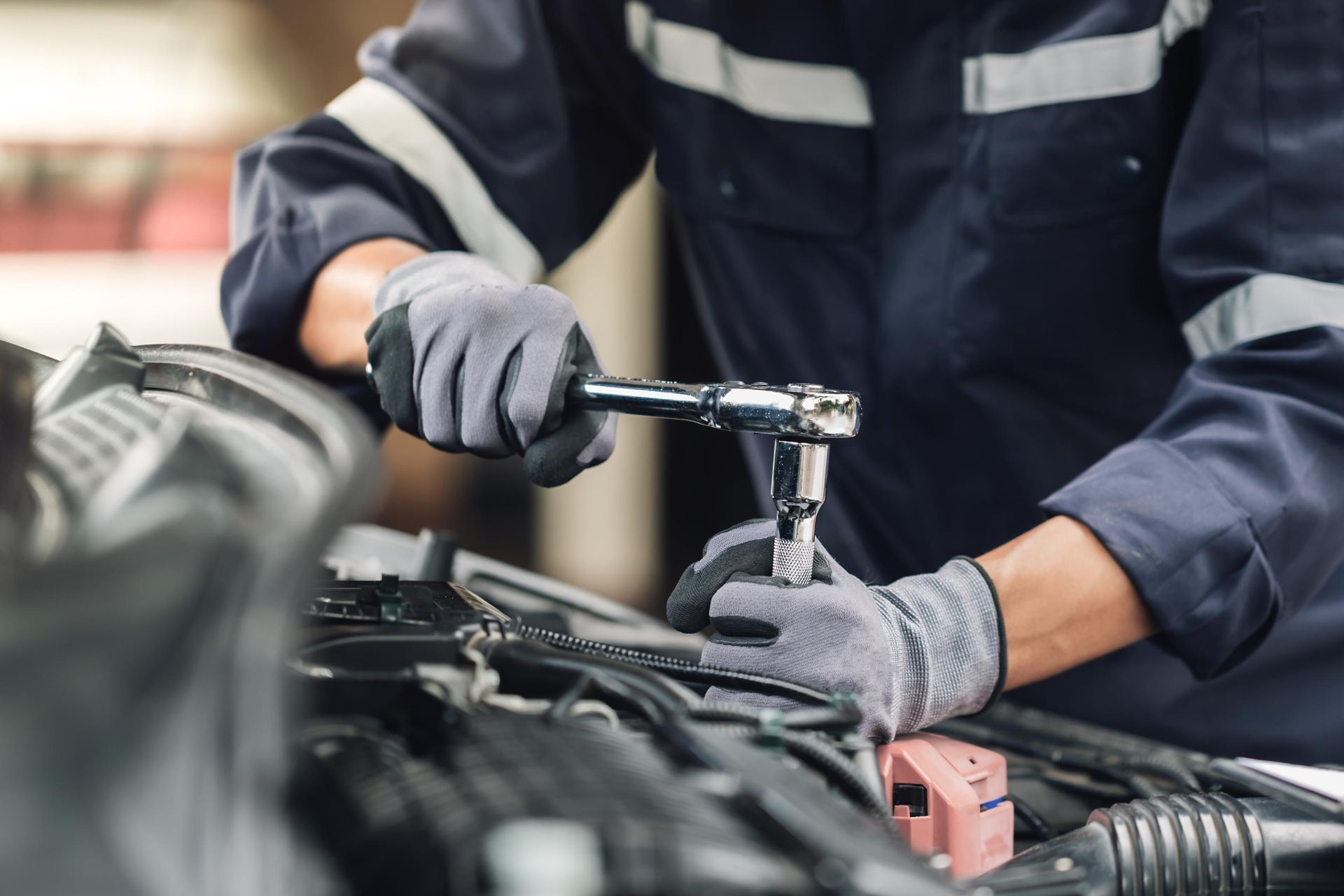 Mechanic in gray gloves using a wrench to repair car engine in a garage