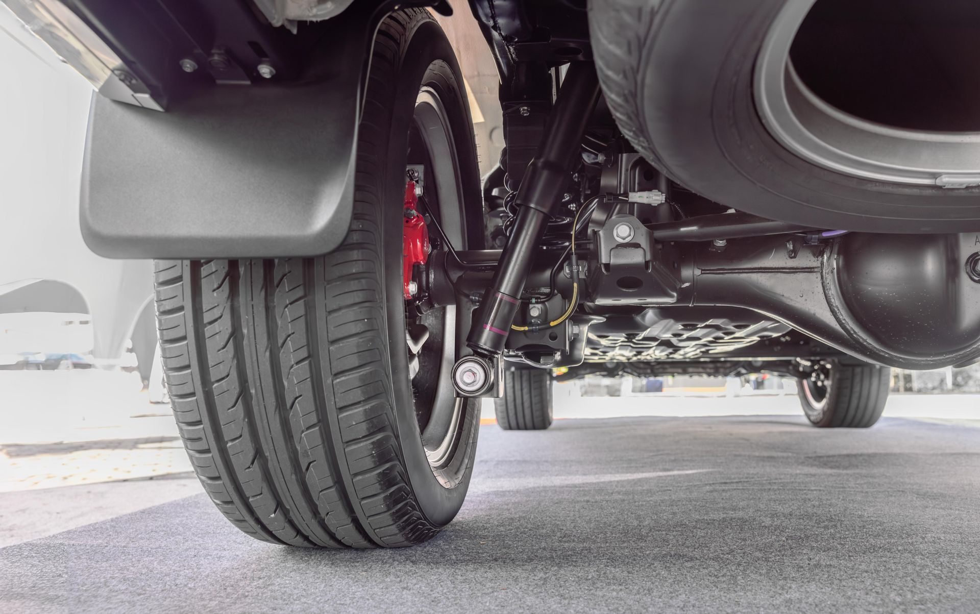 Low-angle view of a vehicle’s front wheel, suspension, and underside on a road.