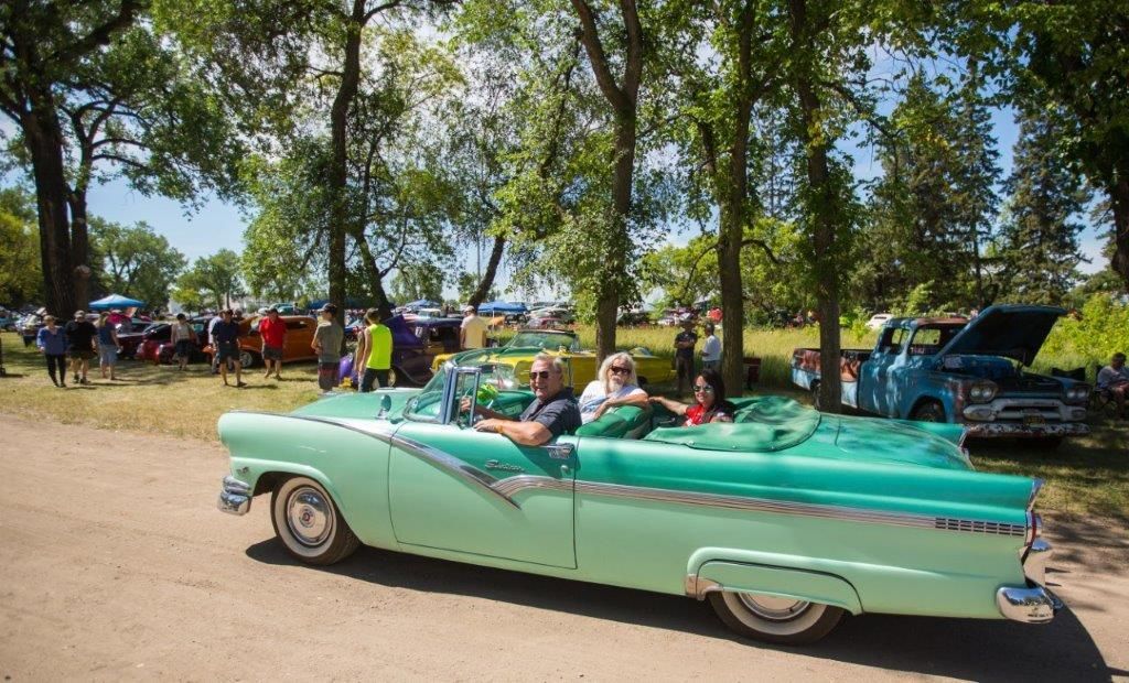 A group of people are sitting in a green convertible car at a car show.