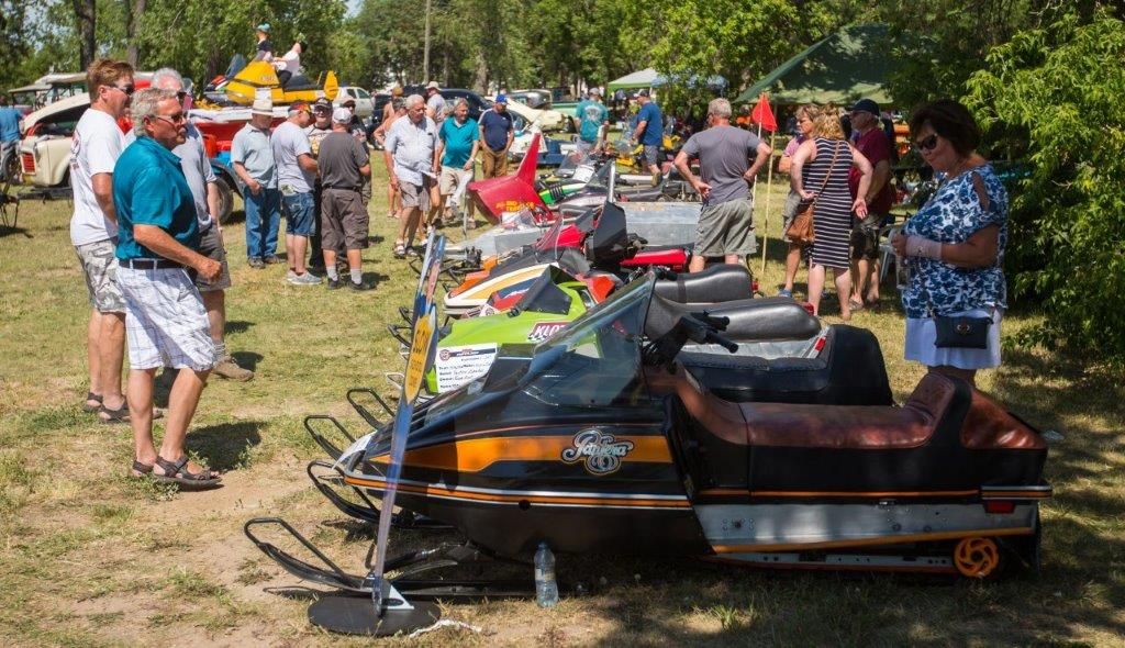 A group of people are standing around a row of snowmobiles.