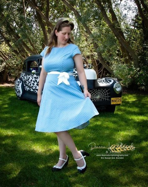 A woman in a blue dress is standing in front of a car