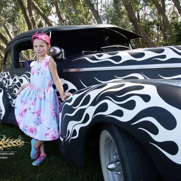 A little girl standing next to a black and white car with flames on it