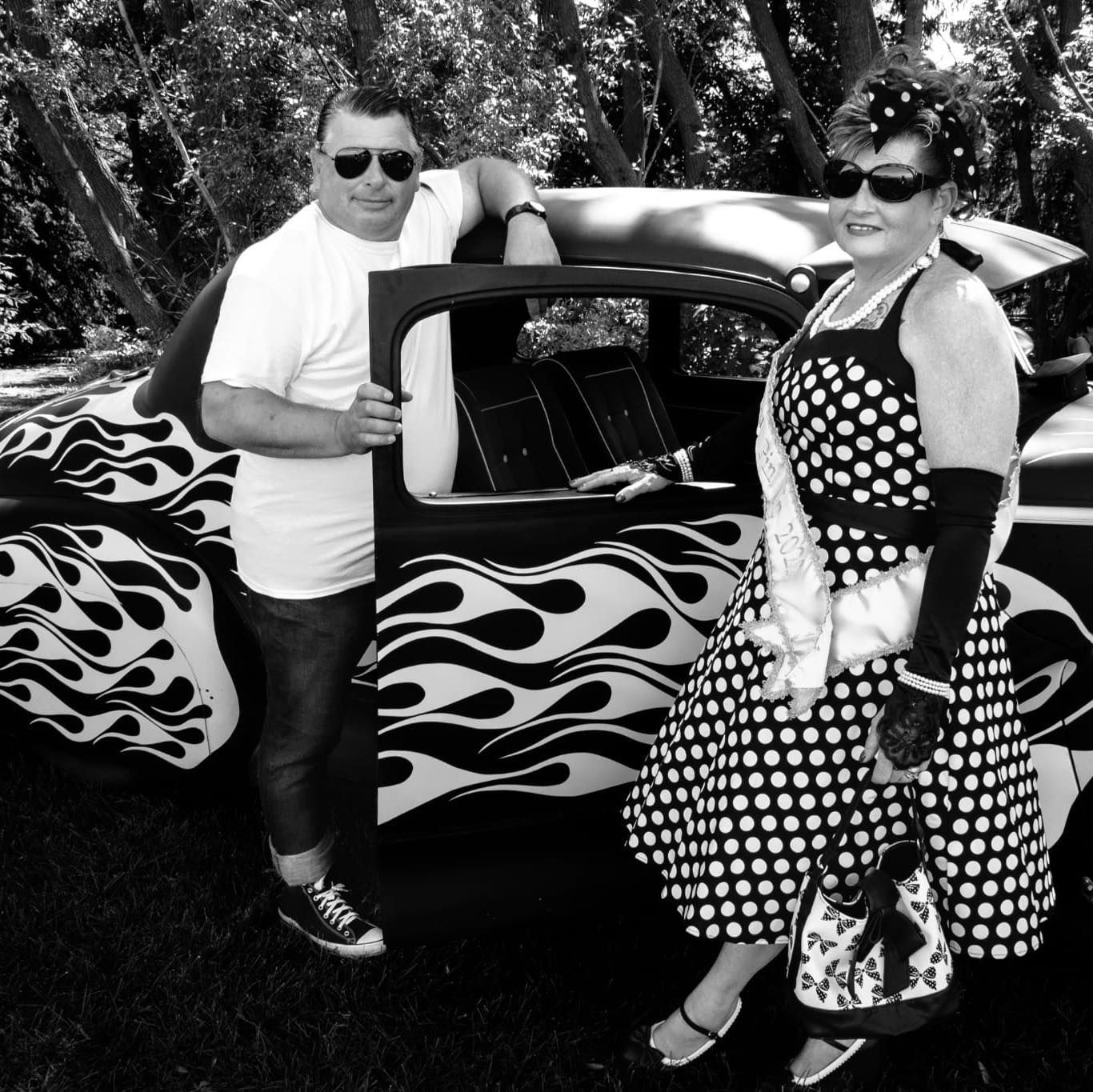 A man and a woman standing next to a car with flames painted on it