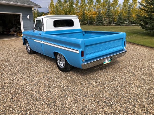 A blue and white truck is parked in a gravel driveway in front of a garage.