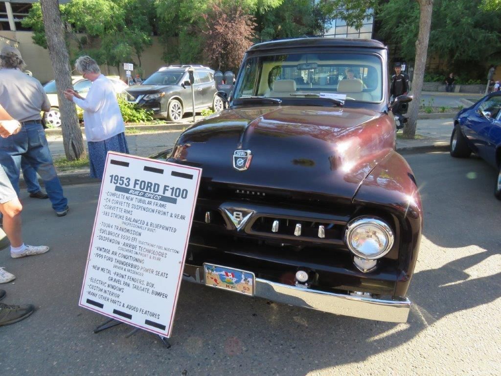 A black ford truck is parked next to a sign that says 1952 ford f100