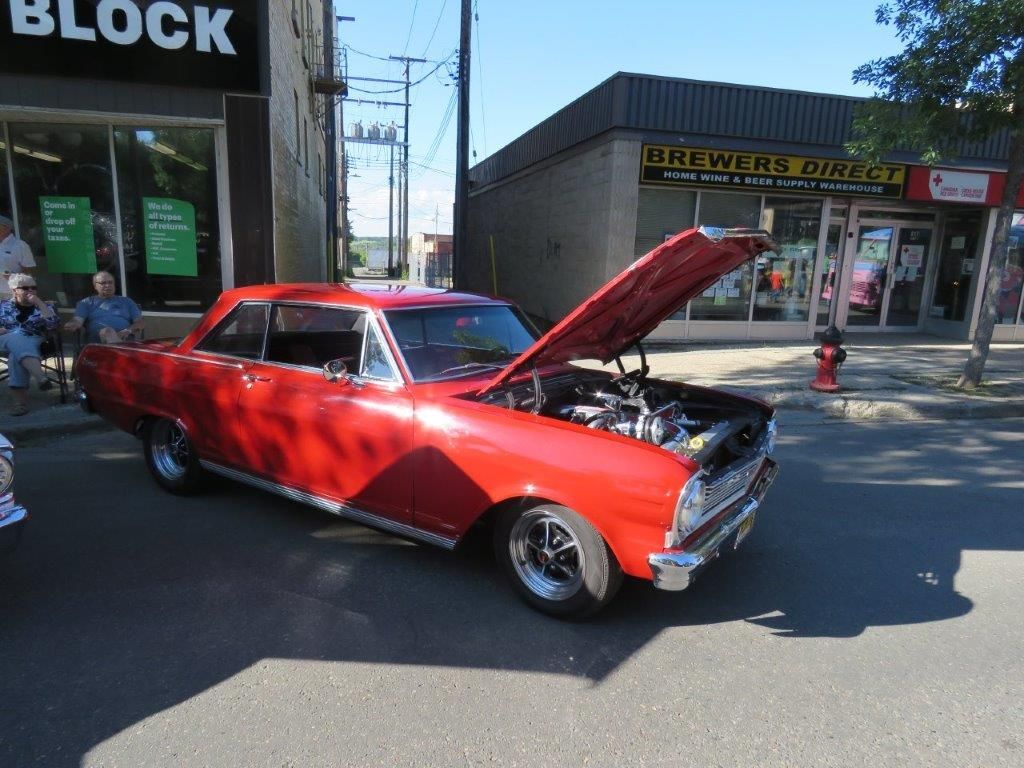 A red car with the hood up is parked on the side of the road