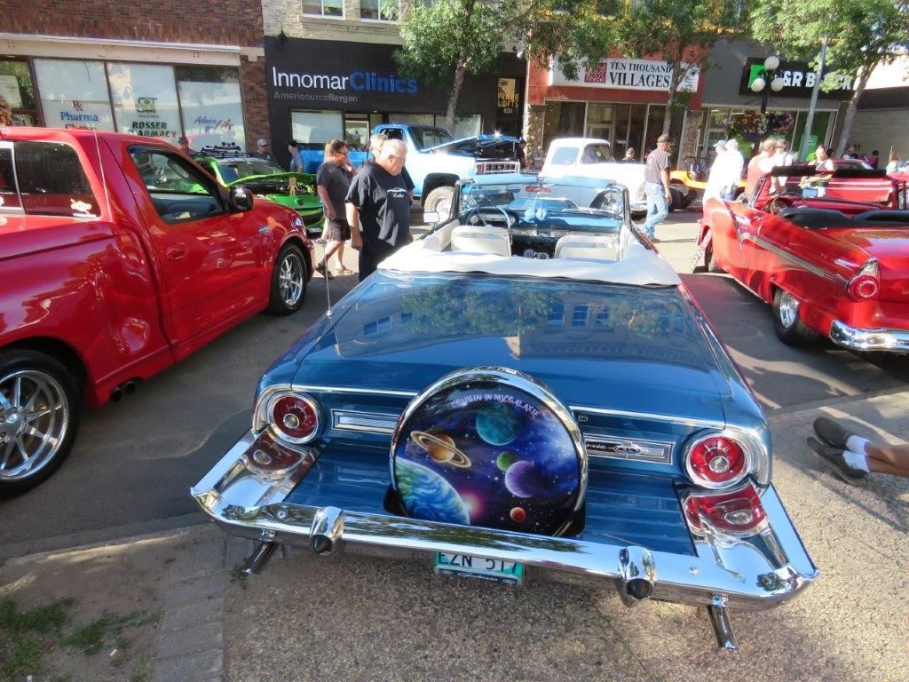 A blue car with a galaxy painted on the back is parked next to a red truck.