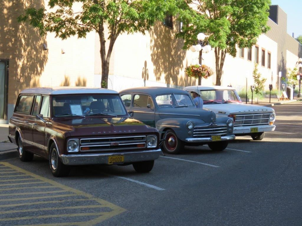 Three old cars are parked on the side of the road