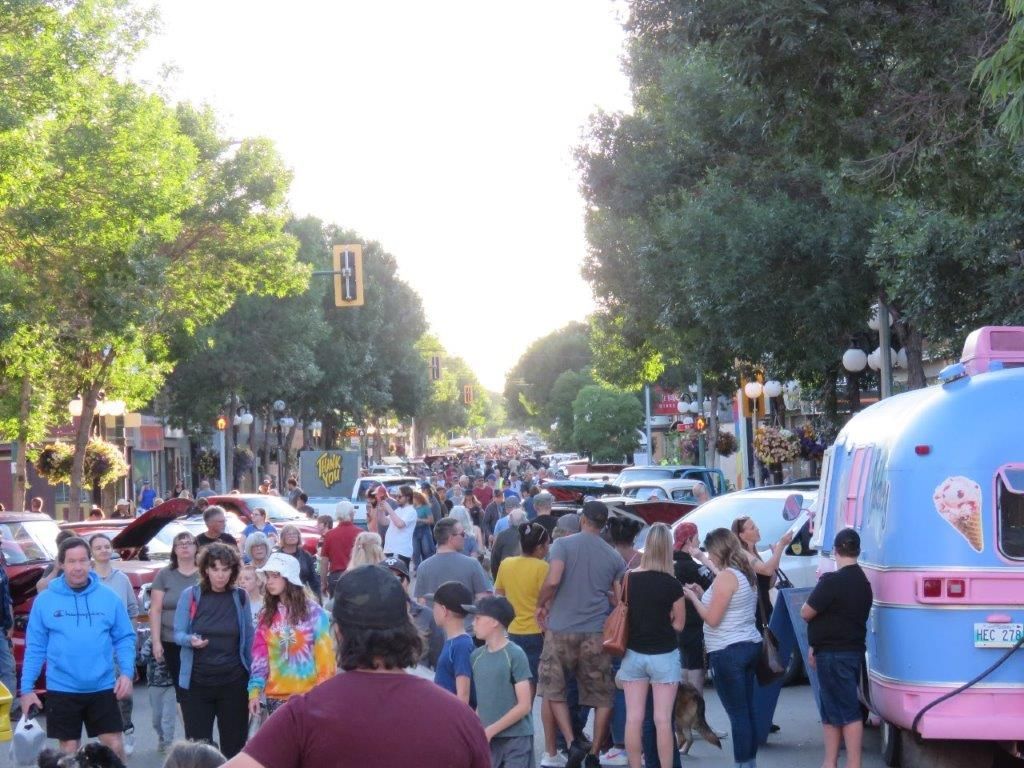 A crowd of people are walking down a street next to a pink ice cream truck.