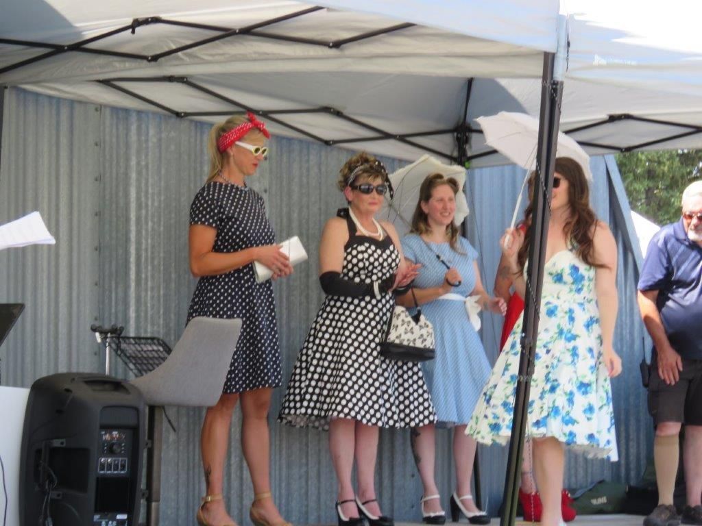 A group of women in dresses are standing under a tent.