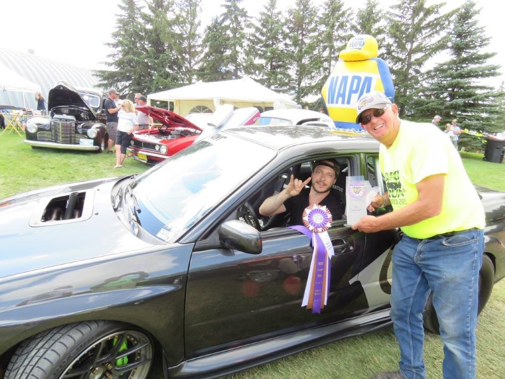A man is giving a trophy to a man in a car at a car show.