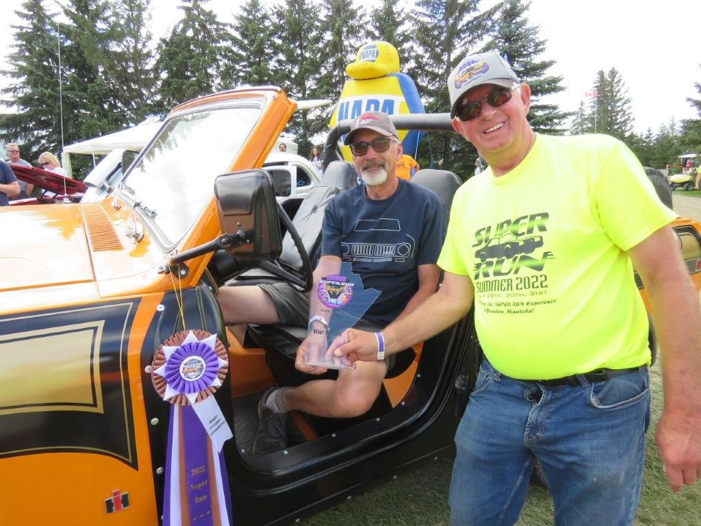 Two men are standing next to a car at a car show.