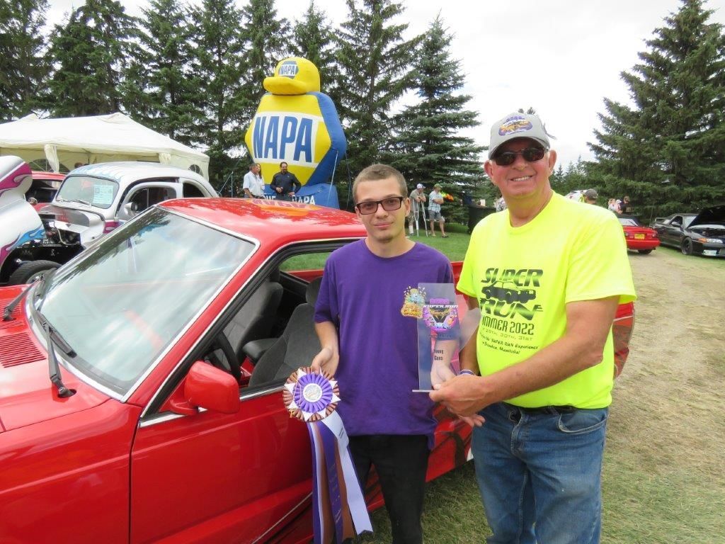 Two men are standing in front of a red napa car