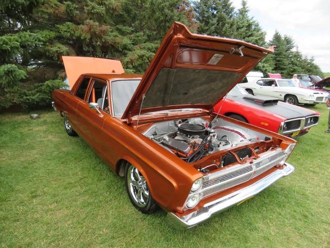 A brown car with the hood up is parked in the grass at a car show.