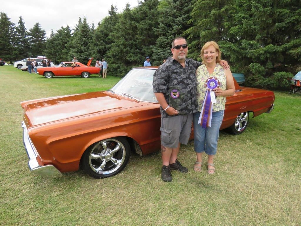 A man and a woman are standing next to a car at a car show.