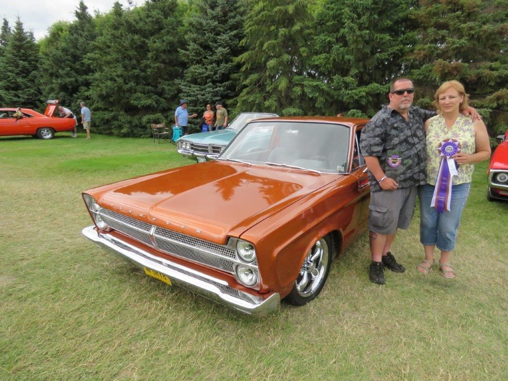 A man and a woman are standing next to a car at a car show.