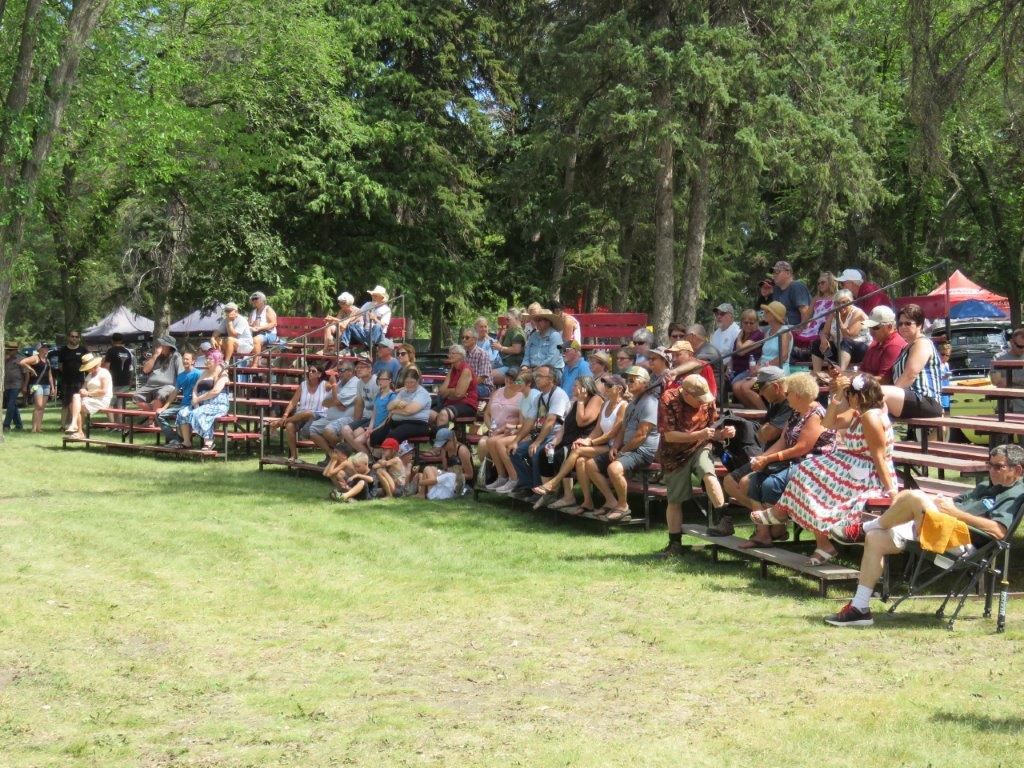 A large group of people are sitting on bleachers in a park.