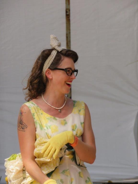 A woman in a yellow dress and yellow gloves is smiling.