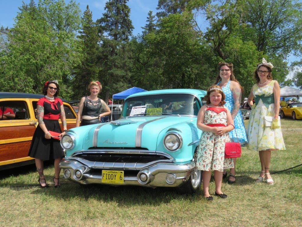 A group of women are standing in front of a blue car.